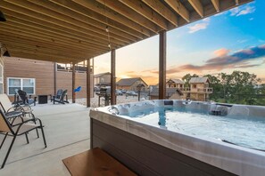 A covered outdoor area with a hot tub, lounge chairs, and a view of surrounding buildings.