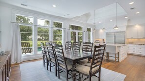 A spacious kitchen with white cabinets, a large island, and a dining area with a wooden table and chairs. - Luxury Sea Pines Sanctuary • Pool • Spa • Peaceful Lawn• Golf View (Hilton Head Island)