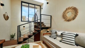A modern living space with a staircase, a sofa with striped pillows, a round table with plants, and a wall-mounted mirror. - Dhalia -Private roof with pool & Beach Club Access (Tulum)
