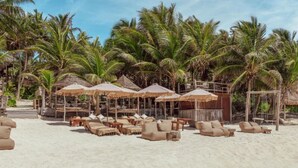 A beachside resort with lounge chairs, thatched umbrellas, and palm trees. - Dhalia -Private roof with pool & Beach Club Access (Tulum)