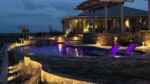 A pool area with a stone wall, lounge chairs, and a covered patio. - TuscanyNTexas (La Grange)