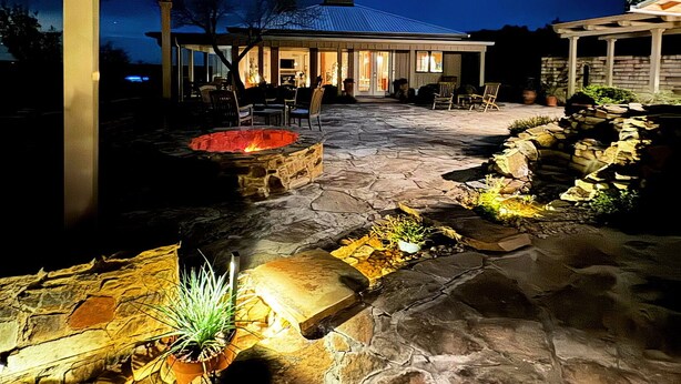 A stone patio with outdoor seating and a fire feature. - TuscanyNTexas (La Grange)