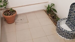 Un petit espace extérieur carrelé, agrémenté d’une plante en pot, d’un petit banc et d’un mur carrelé orné d’un motif décoratif.