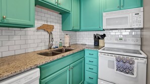 Een keuken met turquoise kastjes, een witte magnetron en een granieten aanrecht.