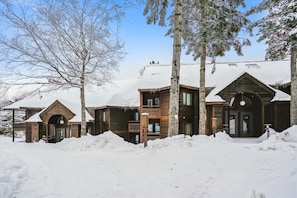A wooden cabin with a snow-covered roof, surrounded by trees.