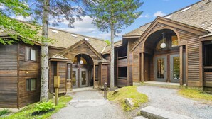 A wooden cabin-style building with multiple entry doors, a gravel pathway, and surrounding greenery.
