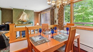 A dining area with a wooden table set for four, a chandelier, and a view of greenery outside.