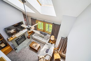 Una sala de estar moderna con chimenea, ventilador de techo, sofá, mesa de centro y vistas al exterior.
