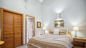 Une chambre à coucher avec un grand lit, deux tables de chevet avec des lampes, une armoire en bois et un espace douche.