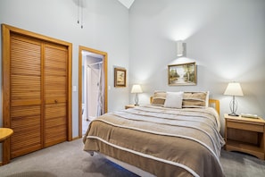 Een slaapkamer met een groot bed, twee nachtkastjes met lampen, een houten garderobe en een douche.