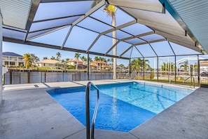 Piscina com guarda-corpo de metal, rodeada por área coberta com telhado de metal e paredes de vidro.