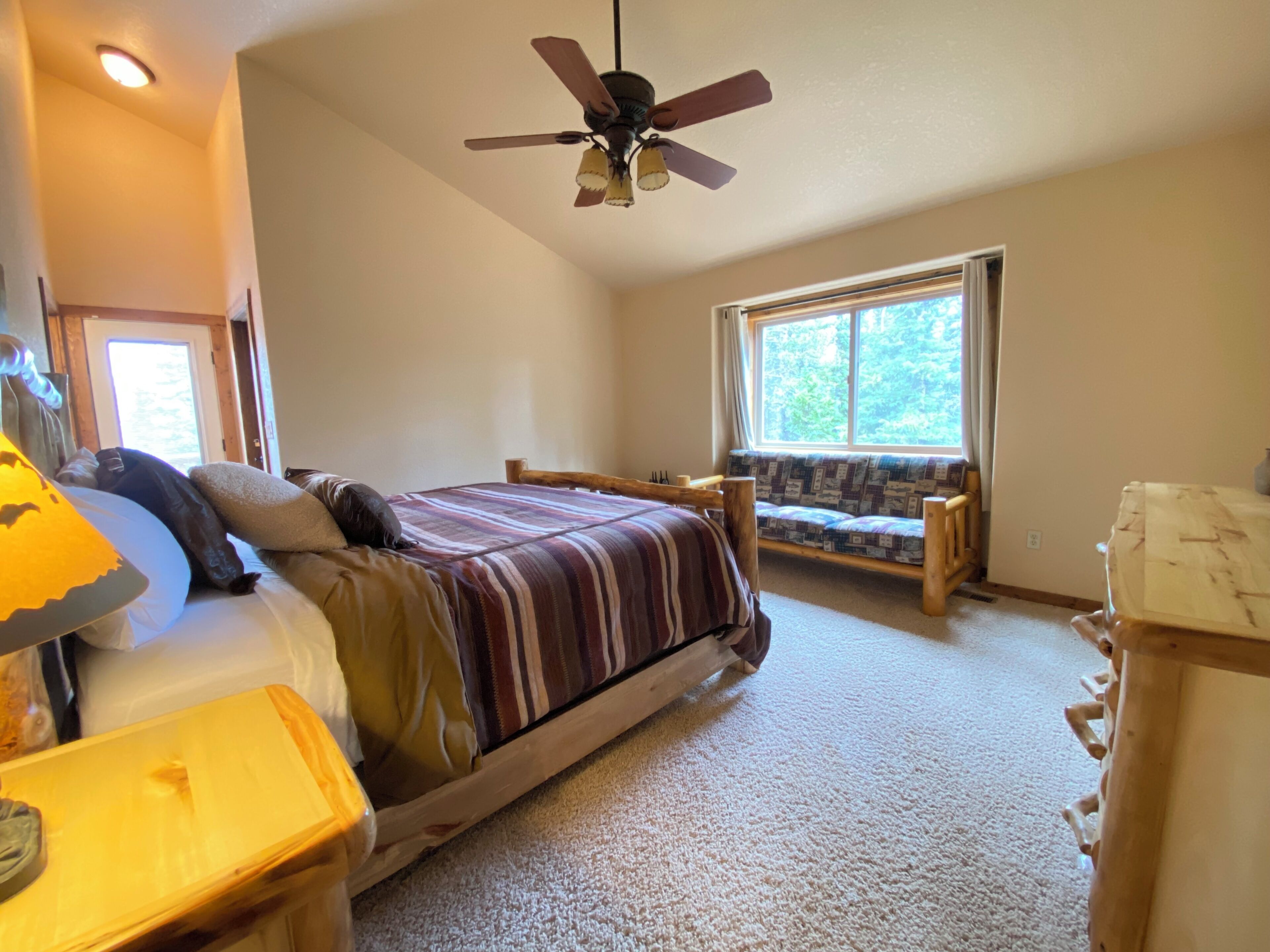 A bedroom with a bed, a wooden bench, a ceiling fan, a window, and a lamp.
