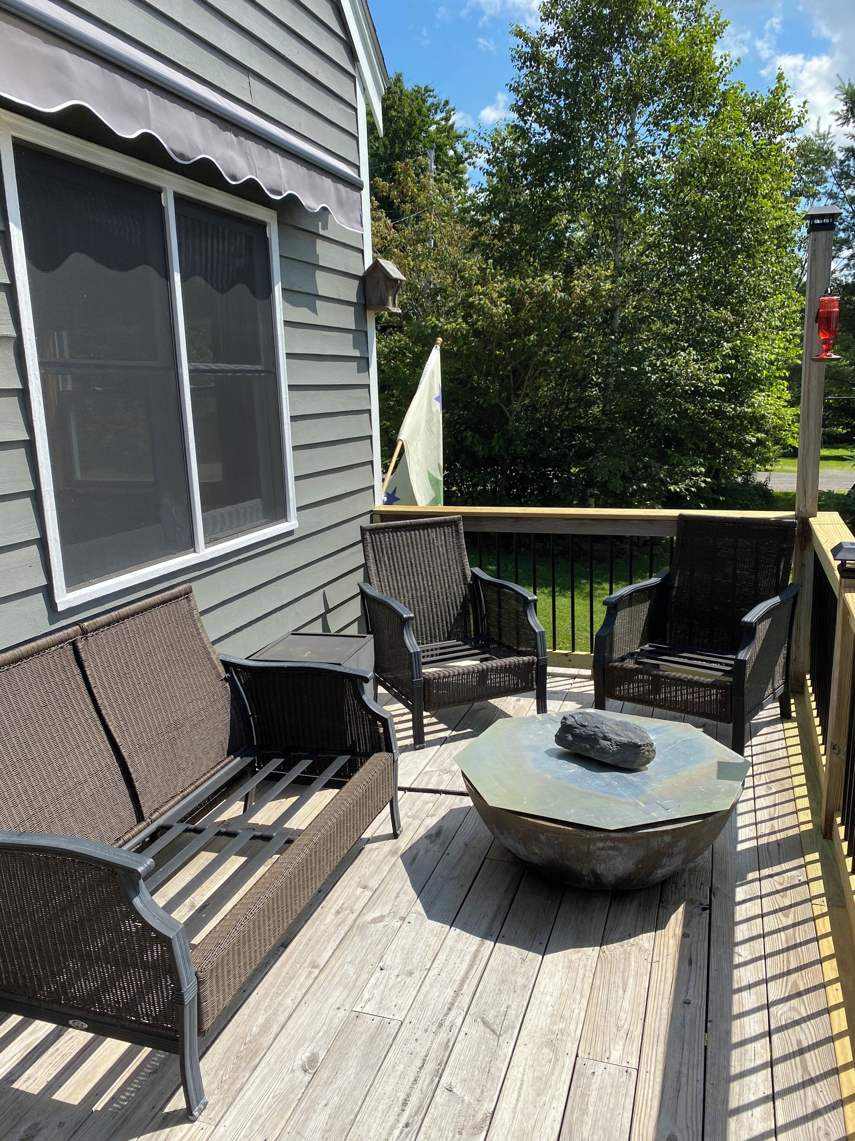 Une terrasse en bois agrémentée de meubles en osier, notamment d’un canapé et de fauteuils, ainsi que d’une table en pierre.