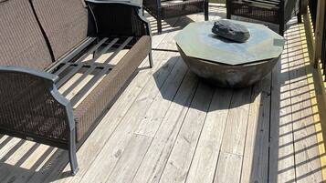 Une terrasse en bois agrémentée de meubles en osier, notamment d’un canapé et de fauteuils, ainsi que d’une table en pierre.