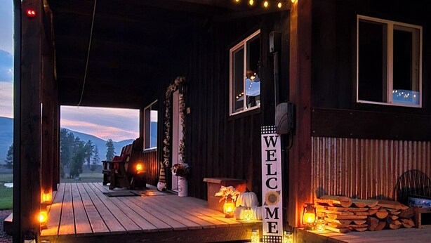 Une cabane en bois dotée d’un porche illuminé par des guirlandes lumineuses, d’une pancarte de bienvenue et d’une allée en gravier.