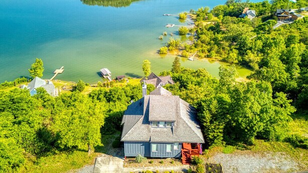 Une maison avec un toit en pente, entourée d’arbres verdoyants et denses, et donnant sur une vaste étendue d’eau.