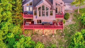 A two-story house with a balcony and a covered deck, surrounded by dense greenery. - Lake View Cabin: Chic Home w/ Panoramic Views (Sevierville)