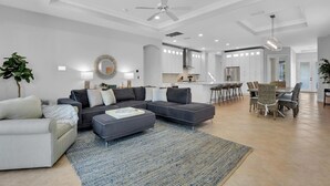 A spacious living room with a grey sectional sofa, a coffee table, and a dining area with a bar. - Ravello by the Beach - Beautiful pool home! (Naples)