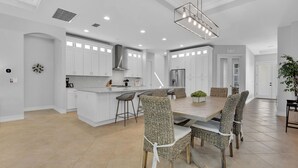 A spacious kitchen with white cabinetry, a central island, and a dining area with wicker chairs and a large table. - Ravello by the Beach - Beautiful pool home! (Naples)