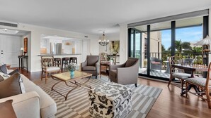 A spacious living room with a large window, a dining area with a table and chairs, and a kitchen visible through an open door. - Beachfront delight in the Moorings! (Naples)