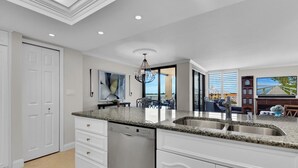 A modern kitchen with white cabinetry, granite countertops, and a Bosch dishwasher. - Beachfront delight in the Moorings! (Naples)