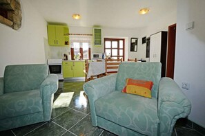 Una sala de estar con dos sillones, un sofá, una zona de cocina con armarios verdes, una mesa de comedor y una ventana con cortinas.