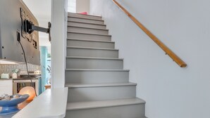 Eine Treppe mit einer Holzhandläufe, ein Küchenbereich mit Herd und Schränken sowie eine blaue Schüssel auf der Arbeitsfläche.