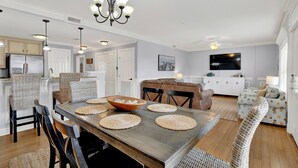 Eine moderne Küche mit weißen Schränken, ein Essbereich mit Holztisch und ein Wohnzimmer mit Sofa und Fernseher.