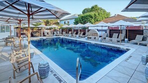 Ein Swimmingpool mit Liegestühlen und Sonnenschirmen, umgeben von einer Steinmauer und einem Gebäude im Hintergrund.