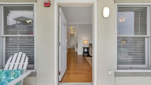 Un pasillo que conduce a una habitación con suelo de madera, una puerta blanca y una ventana con persianas.