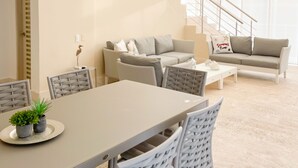 A modern living room with a dining area, a staircase, and large windows.