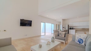 A spacious living area with a flat-screen TV mounted on the wall, a coffee table with decorative items, and a sofa with a decorative pillow.