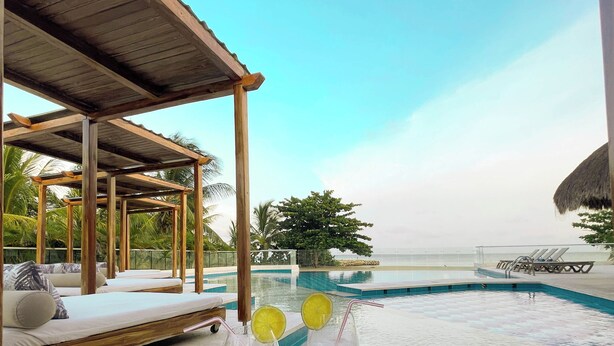 A poolside area with lounge chairs, a wooden pergola, and a table with drinks and a placemat.