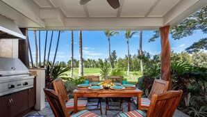 Un patio exterior con una parrilla, mesa de comedor, sillas y vistas a un paisaje tropical.