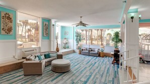 A spacious living room with a large window, a ceiling fan, and a view of palm trees. - Daytona Beach Studio w/ Ocean View + Amenities! (Daytona Beach)