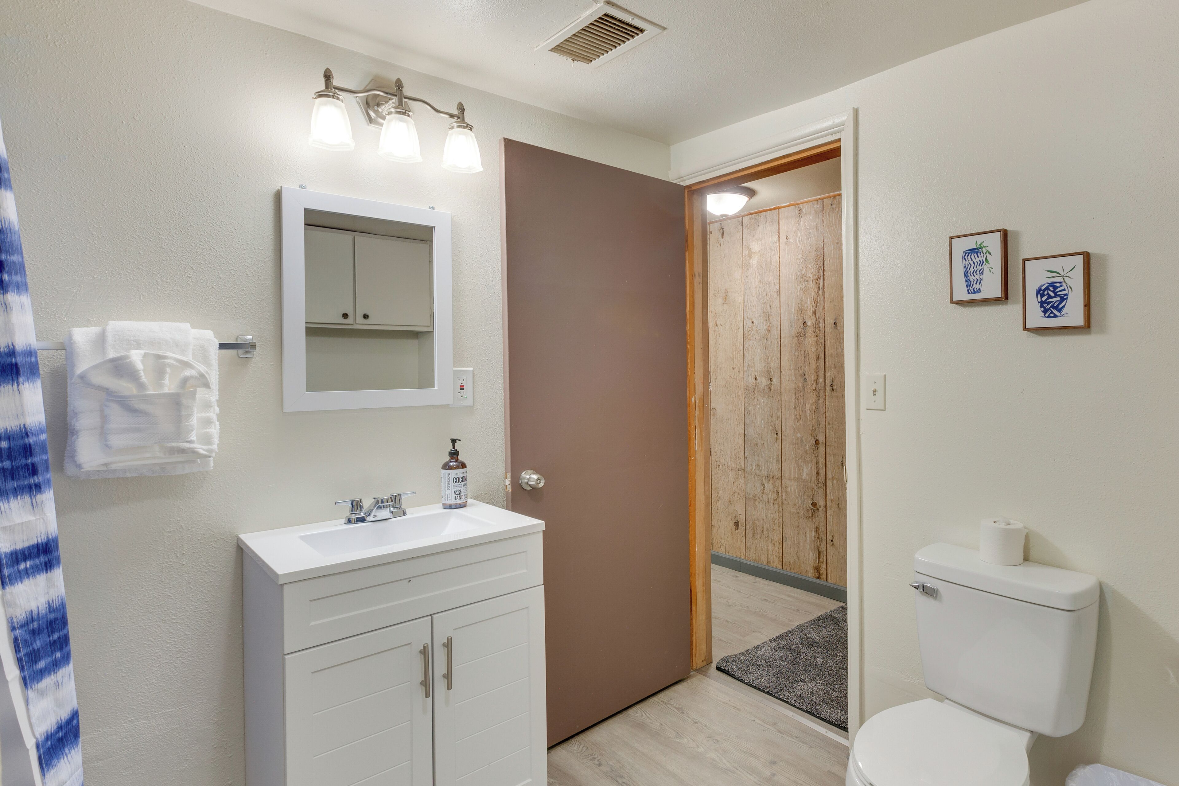 A bathroom with a white sink, mirror, and toilet. There is a wooden door leading to another room.