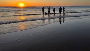 A beach scene with a sunset, people standing by the water, and a dog. - Banksia - EV charger and Linen provided (Venus Bay)