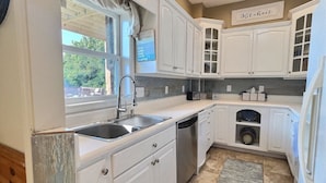 A kitchen with white cabinets, a dishwasher, a sink, and a window with curtains. - Sky Sunset Stay: Mountain Views, Hot Tub, Gameroom (Blue Ridge)