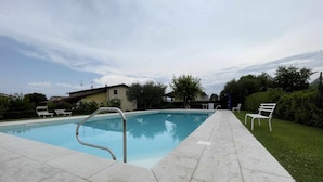 A swimming pool with a tiled deck, a metal ladder, and two white lounge chairs.