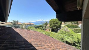 A view from a balcony with a tiled roof, overlooking a landscaped garden and a distant mountain range.