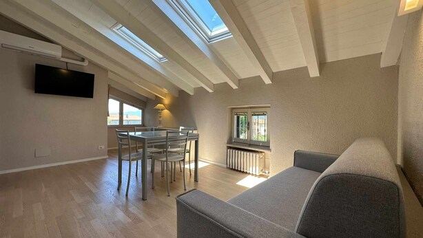 A spacious living area with a high ceiling, skylights, a dining table with chairs, a sofa, and a radiator.