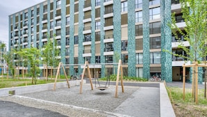 A modern building with a patterned facade, a playground with swings, and a bike parked nearby. - Chic Wollishofen 1BR w/ Storage & W/D, nr Local Market, by Blueground (Zurich)