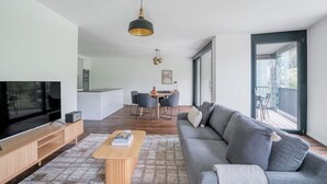 A modern living room with a flat-screen TV, a sofa, a coffee table, and a dining area with chairs and a table. - Chic Wollishofen 1BR w/ Storage & W/D, nr Local Market, by Blueground (Zurich)