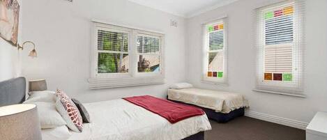 Une chambre avec deux lits, un ventilateur de plafond et des fenêtres équipées de stores.