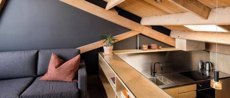 A modern loft apartment with a kitchen, a dark grey sofa, and a wooden ceiling.