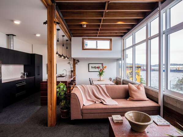 A modern living room with a sofa, a dining table, and a view of the water. - The Thomas Gregg Apartments (Dunedin)