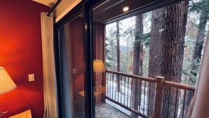 Une pièce dotée d’une grande porte-fenêtre coulissante donnant sur un balcon au sol en pierre et offrant une vue sur de grands arbres.
