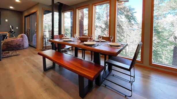 Un coin repas avec une table et des bancs en bois, de grandes fenêtres donnant sur la forêt et un télescope placé dans un coin.