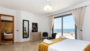 Una habitación de hotel con cama, escritorio, silla, un amplio ventanal con vista al mar y un baño con bañera.