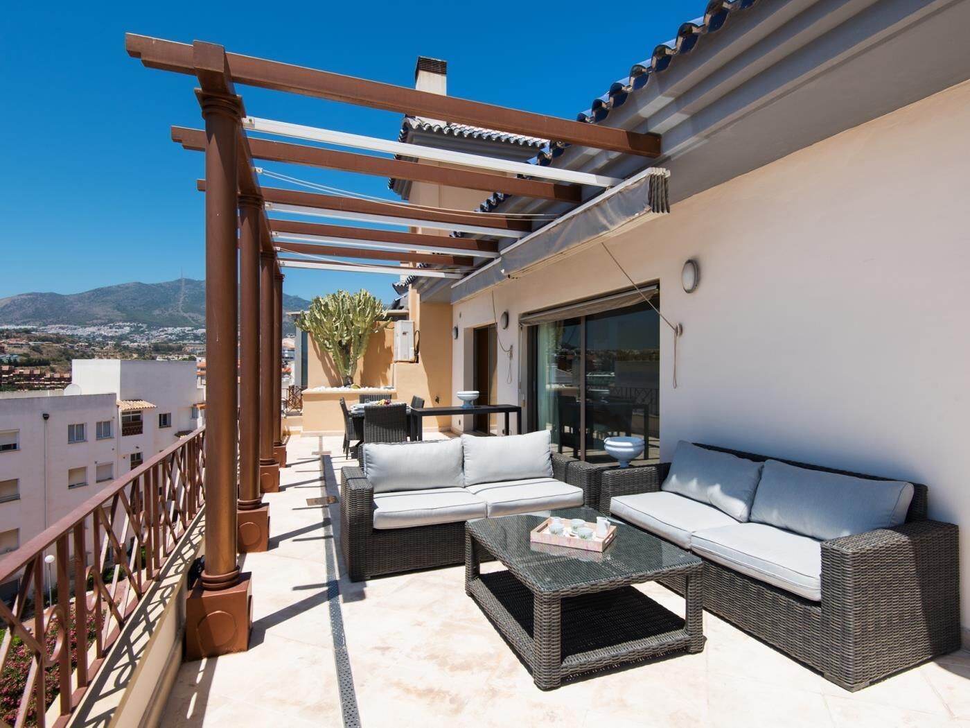 Un balcón con mobiliario exterior, una pérgola y vistas a la ciudad y a las montañas.
